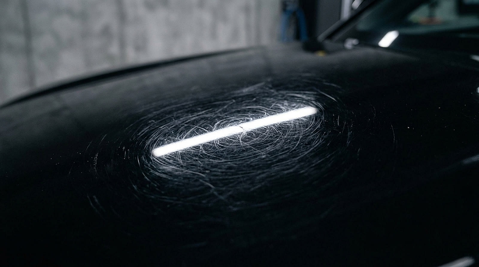 Close-up of black paint with swirl marks under a light bar