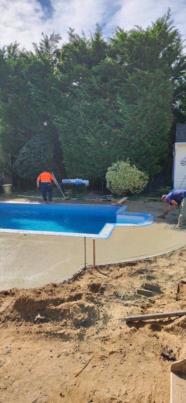 Crew pouring and finishing concrete around the pool