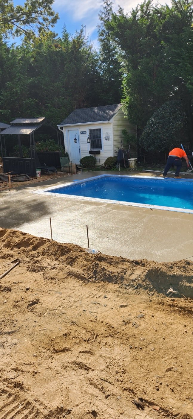 Backyard pool with the ground dug and staked for a new deck